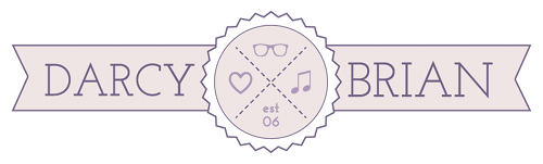 Site logo is light pink with dark purple outline and text. It has a ribbon banner coming straight out on either side of a circle. Left says DARCY. Right says BRIAN. Inside circle are icons for glasses, heart, and music note. It also says est 06.